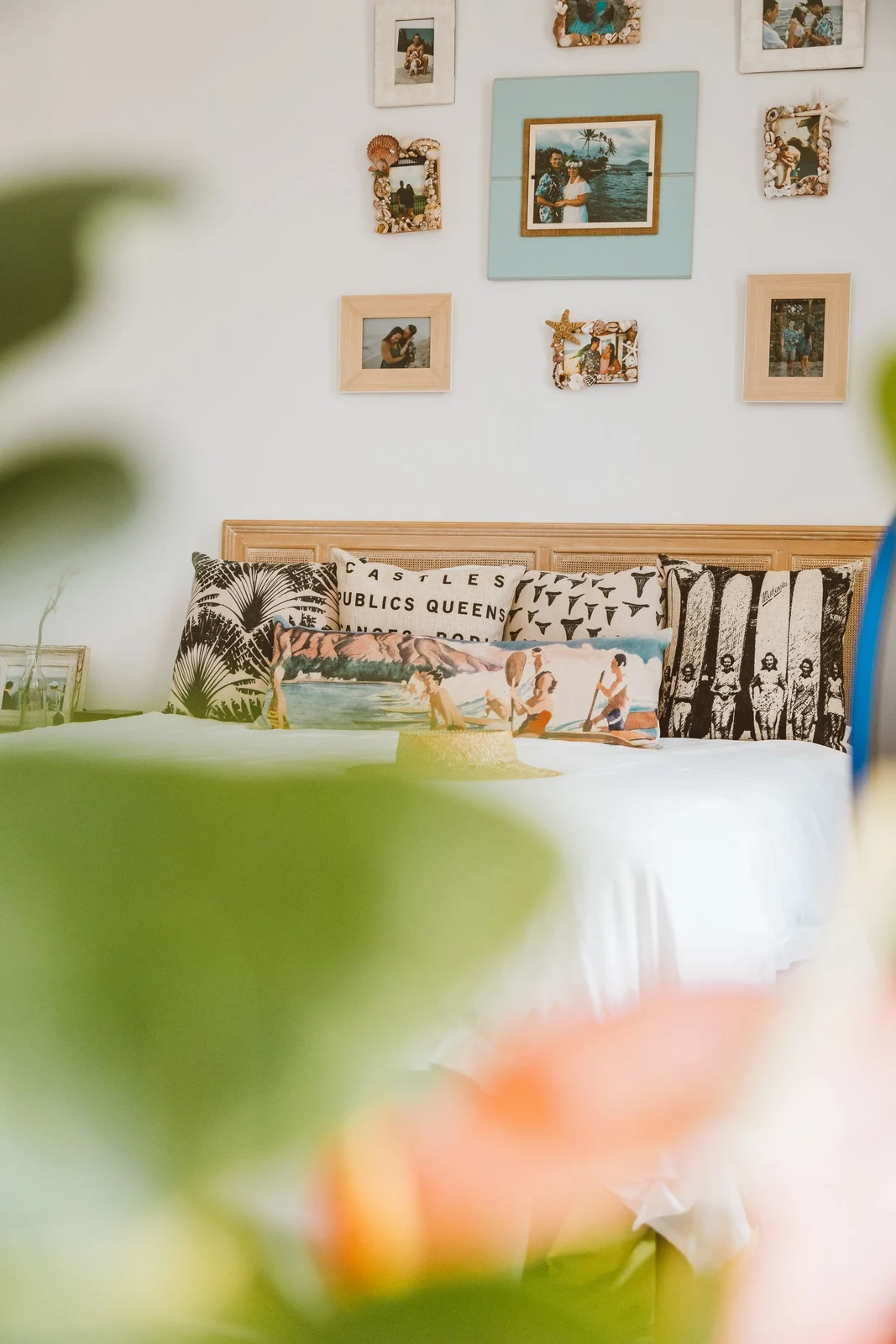 Personal photographs in assorted frames arranged on a white wall above a timber bed