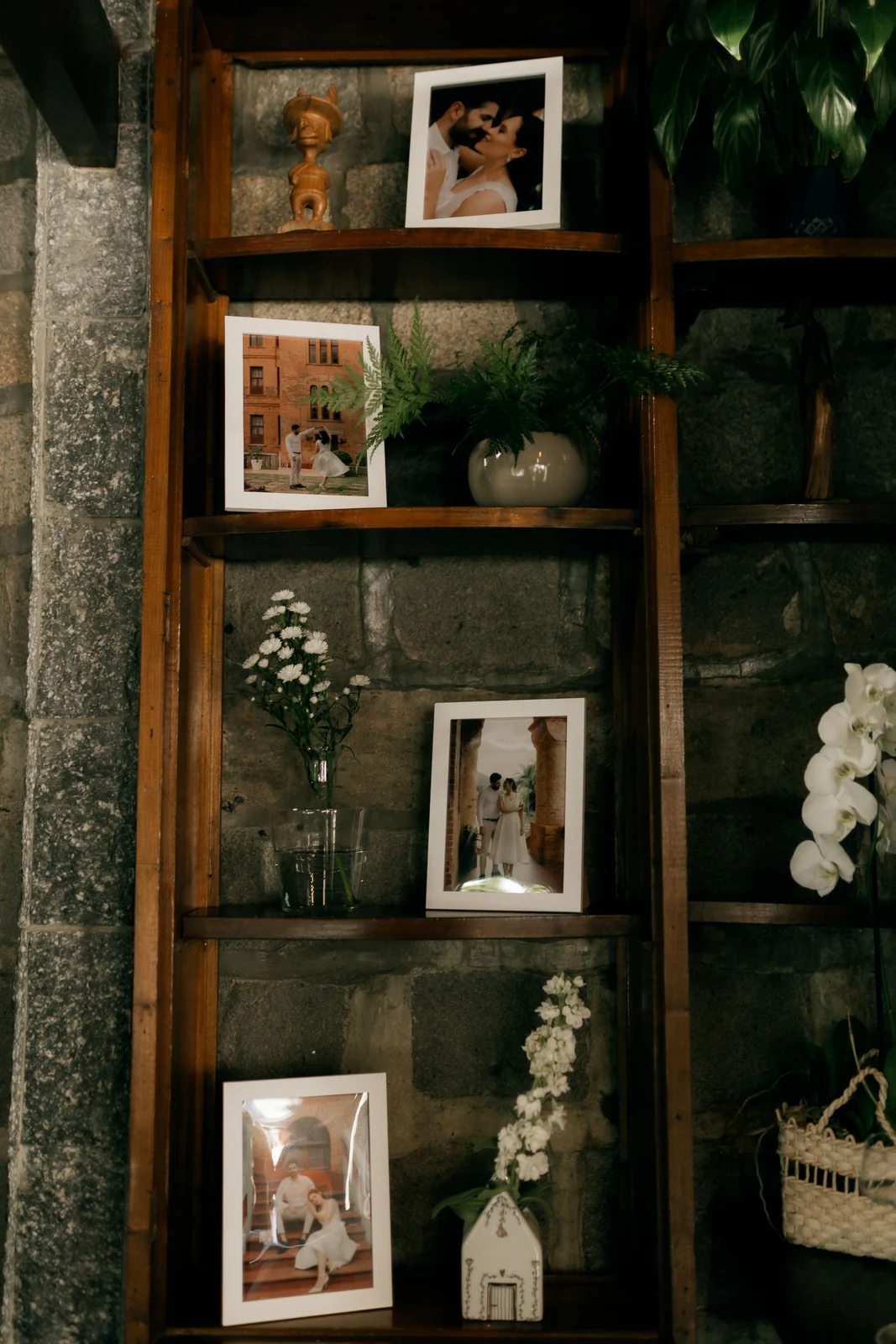 White-framed couple photographs arranged on timber shelves beside flowers and plants