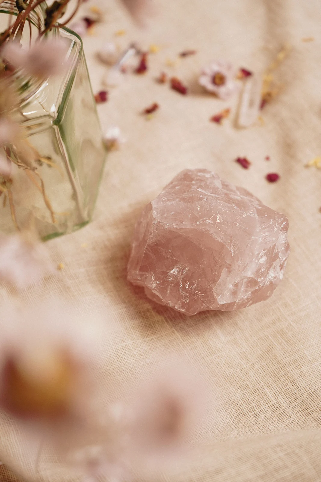 Rough pale pink rose quartz specimen on linen beside a small glass vase