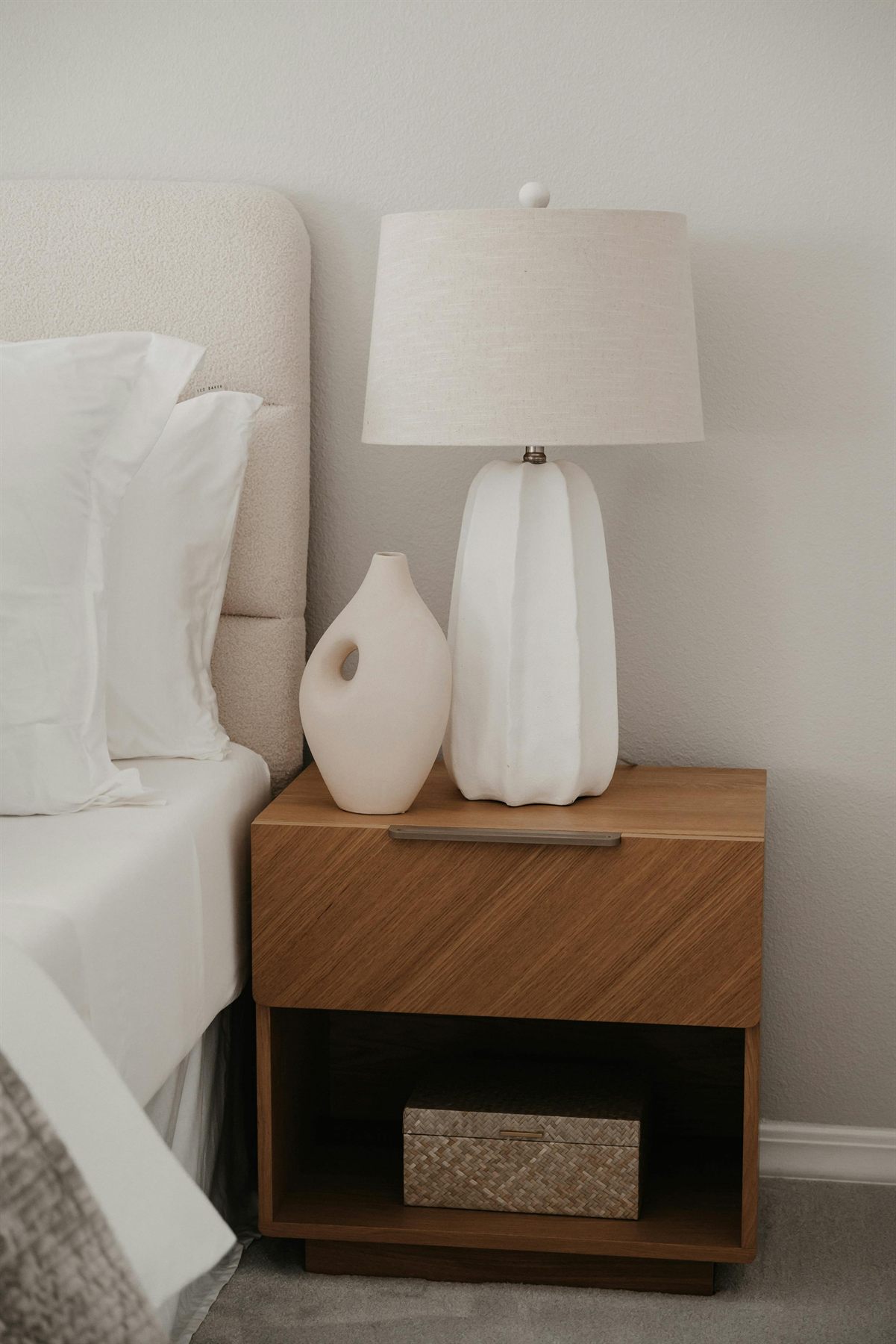 Minimal bedside table with a lamp, wood drawer, and soft bedding