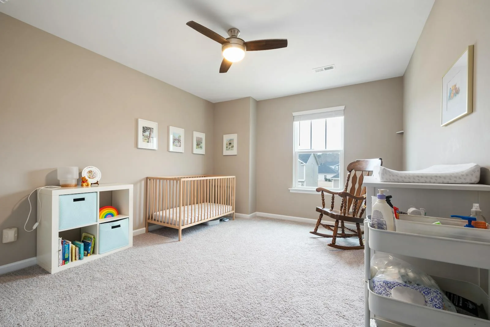 Nursery with beige walls, a light wood crib, cube storage, rocking chair, and changing cart