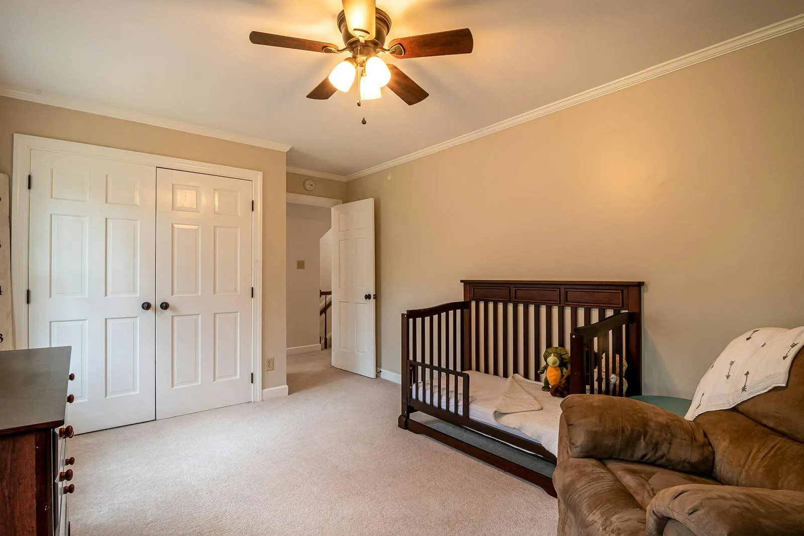 Neutral nursery with a dark wood crib, soft chair, closet doors, and open floor space