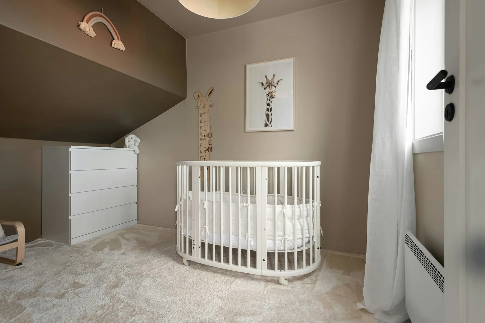 Nursery with a crib, neutral walls, simple shelf styling, and a chair near the window
