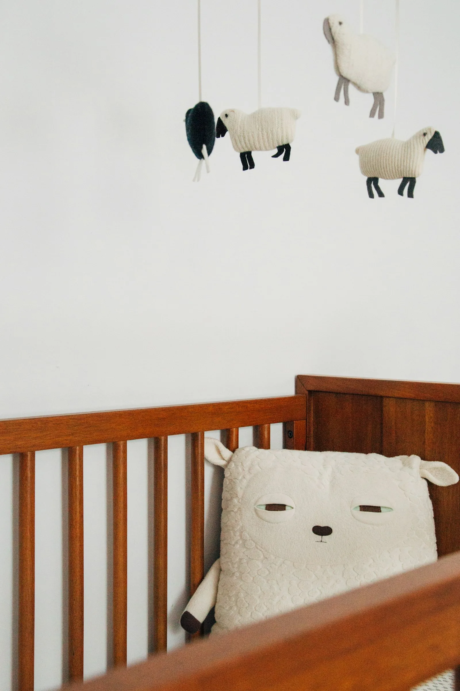 Wood crib with a soft bear pillow and a sheep mobile hanging above in a minimal nursery