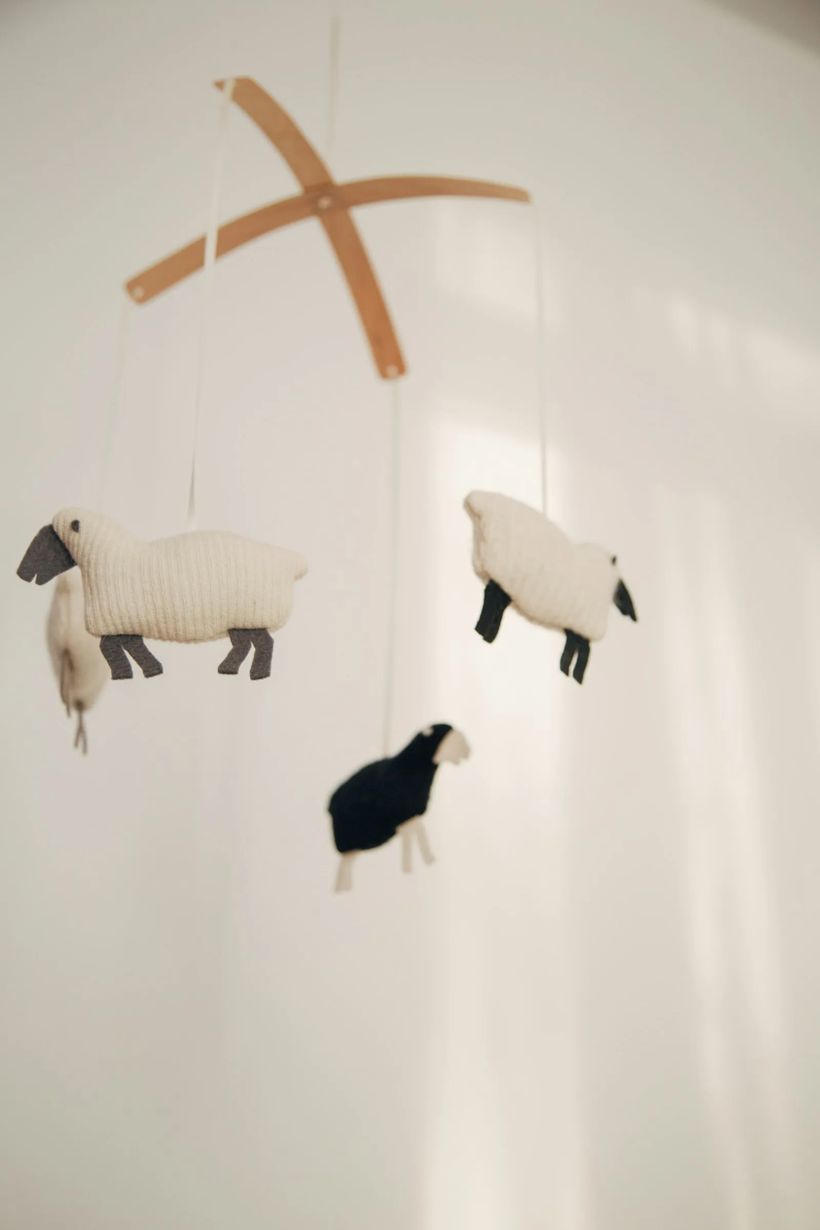 Close view of a soft sheep mobile hanging in warm daylight against a pale wall
