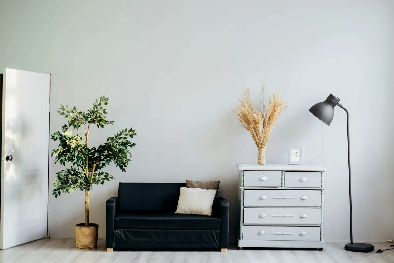 Nursery corner with a black daybed, white dresser, floor lamp, plant, and open space for caregiving