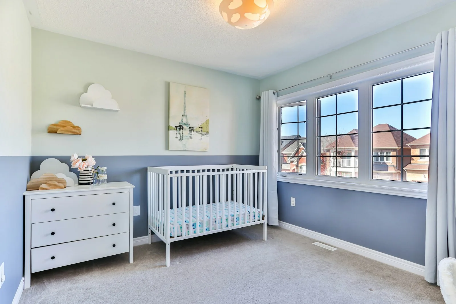 Nursery with a white crib, soft green and blue walls, dresser, and large windows with curtains