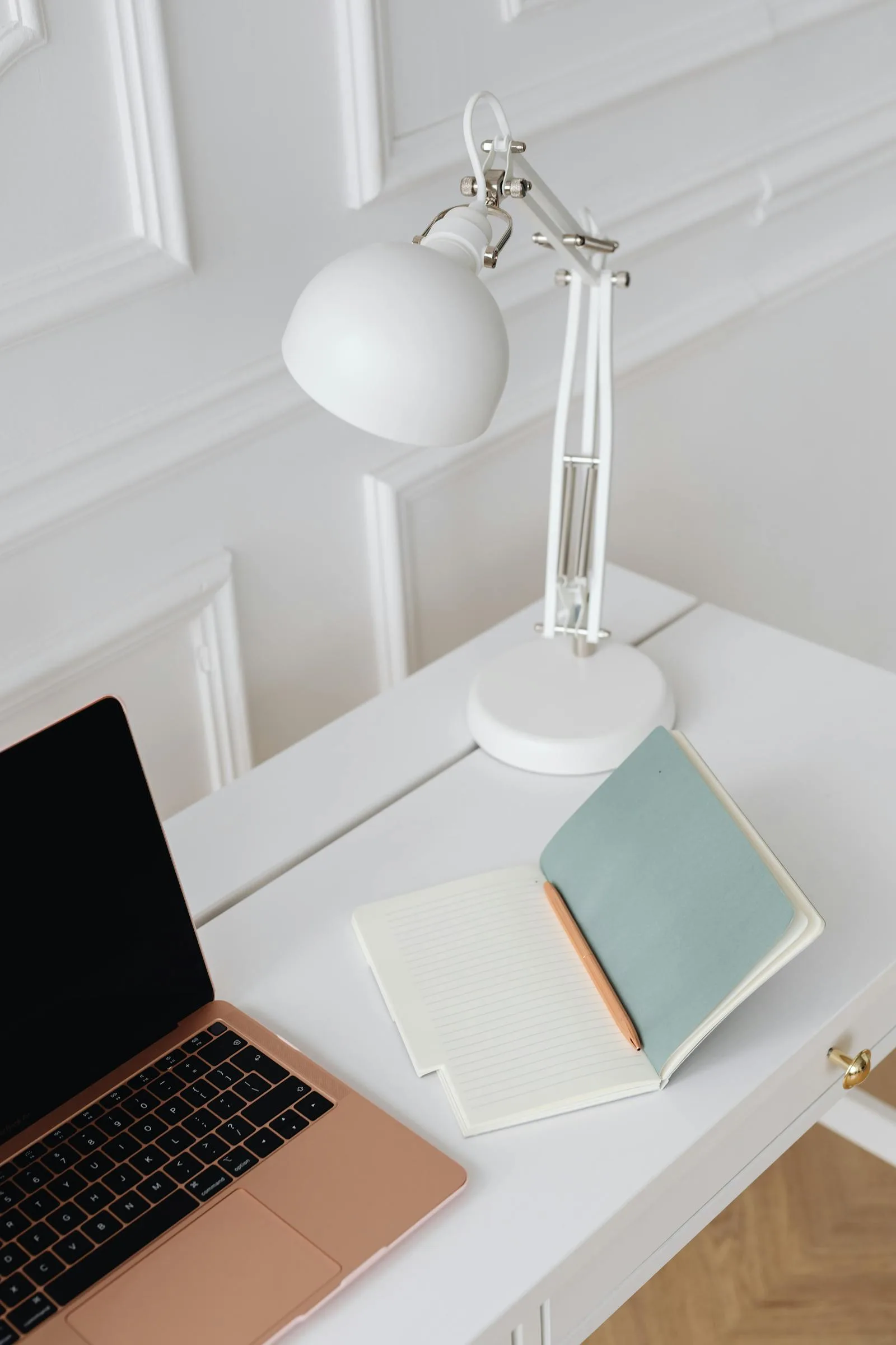 White desk with notebook, lamp, and open work surface