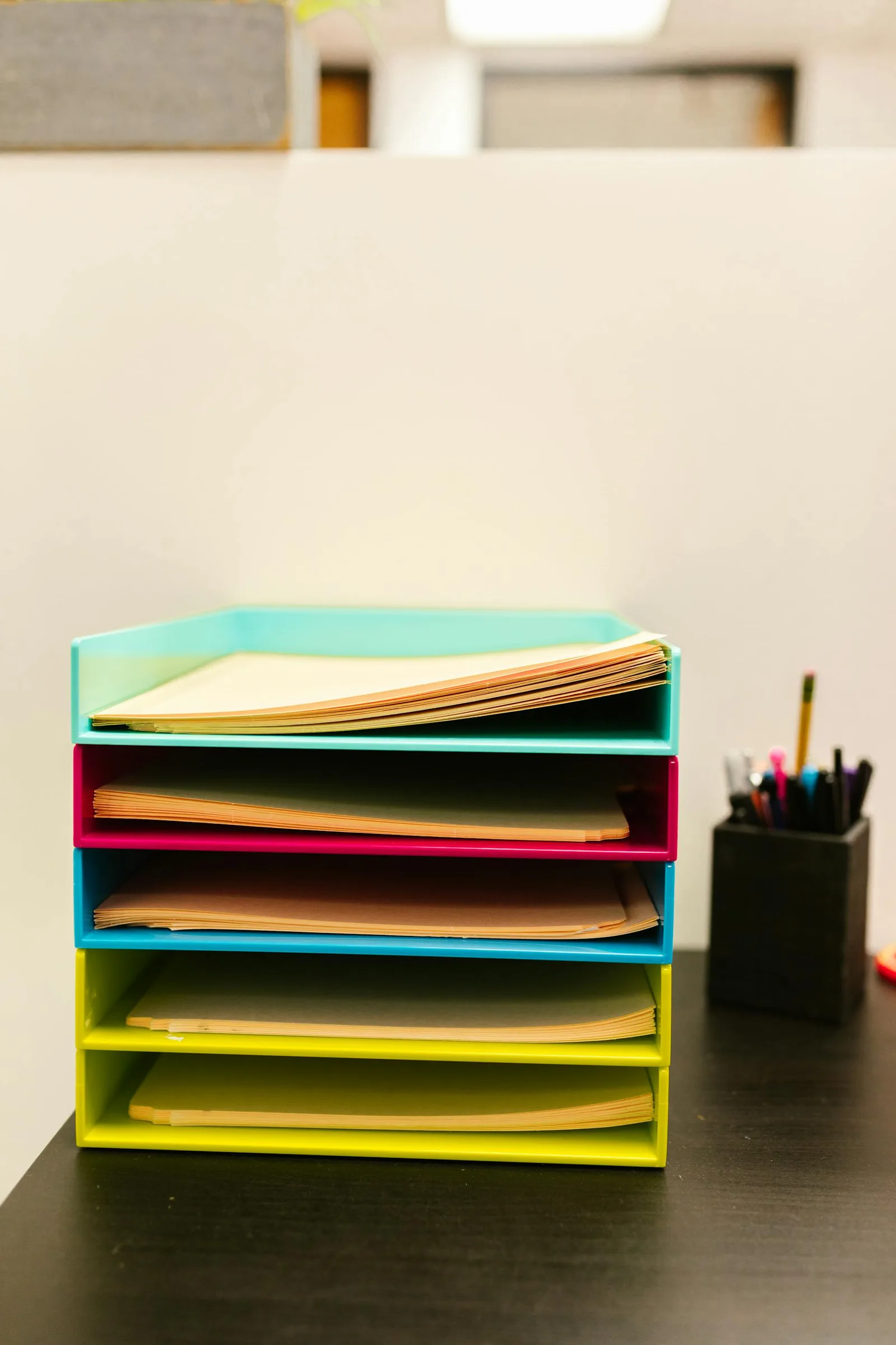 Colorful office paper tray with folders and a pen cup in the background