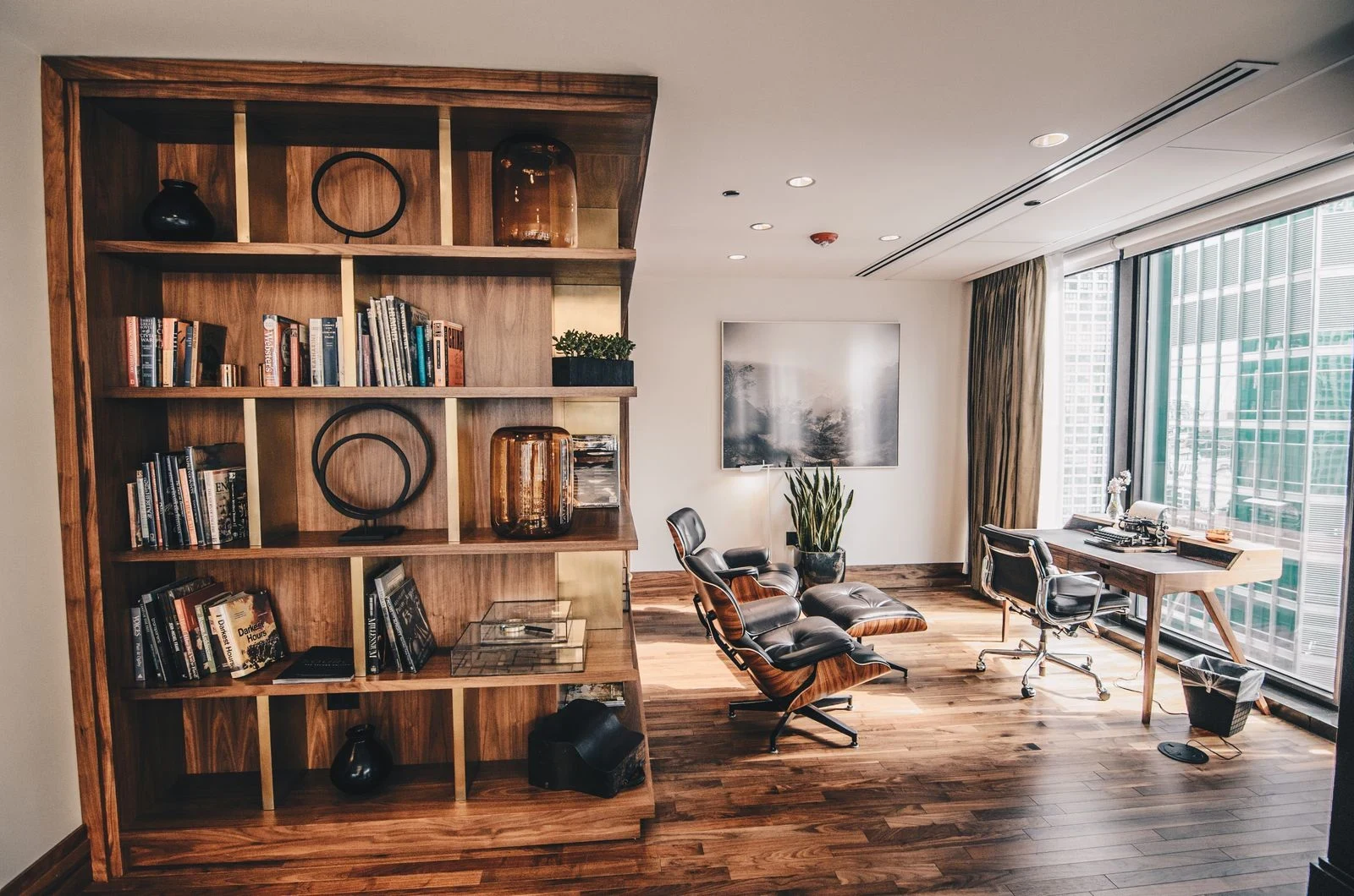 Wooden bookcase beside a study area with a desk, office chair and lounge chair