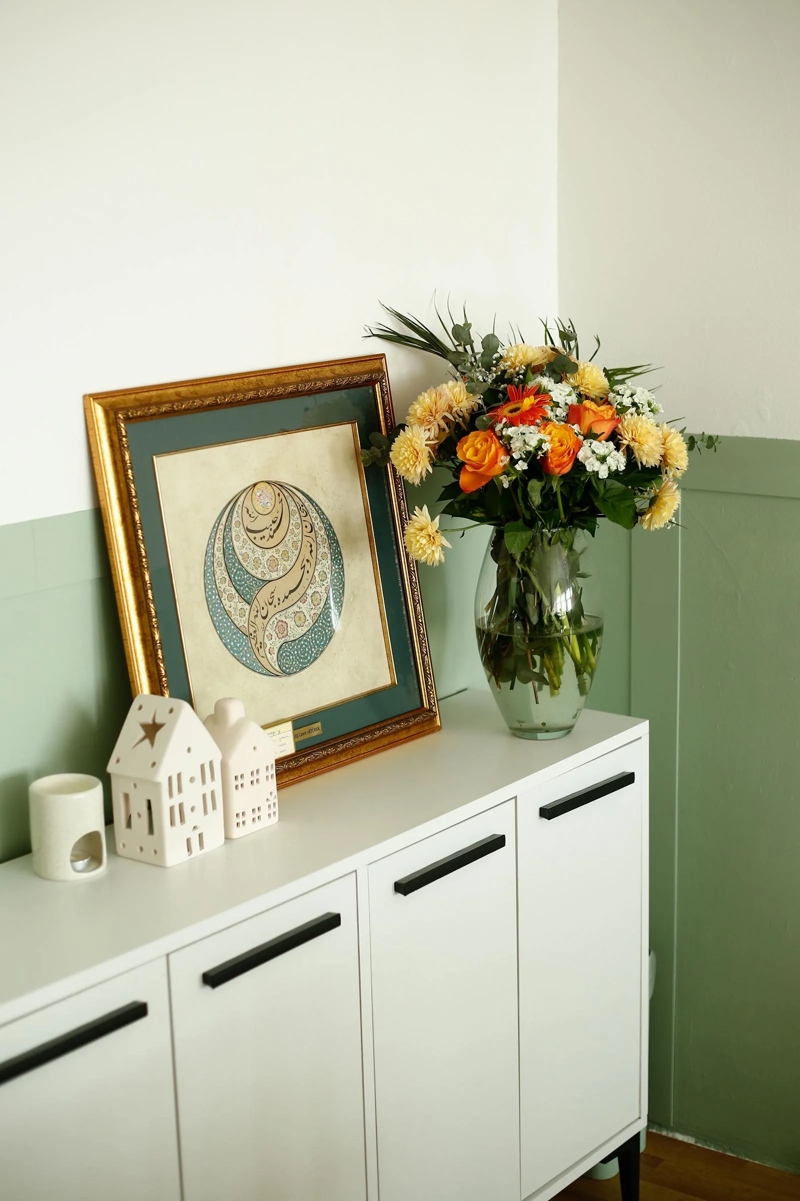 Flowers and framed art on a clean cabinet with a simple edited arrangement