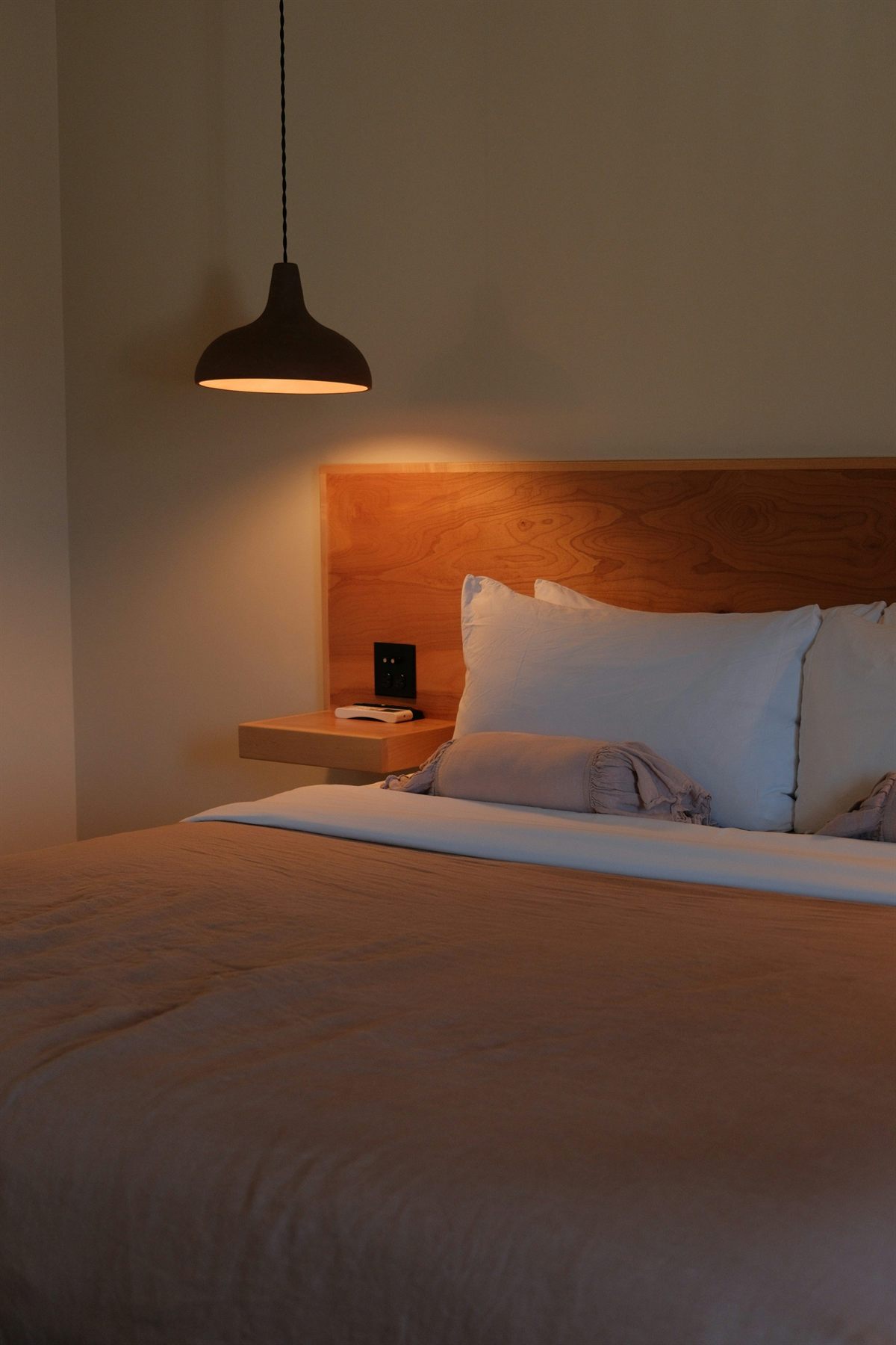 Bedroom with warm pendant light, wood headboard, and soft neutral bedding