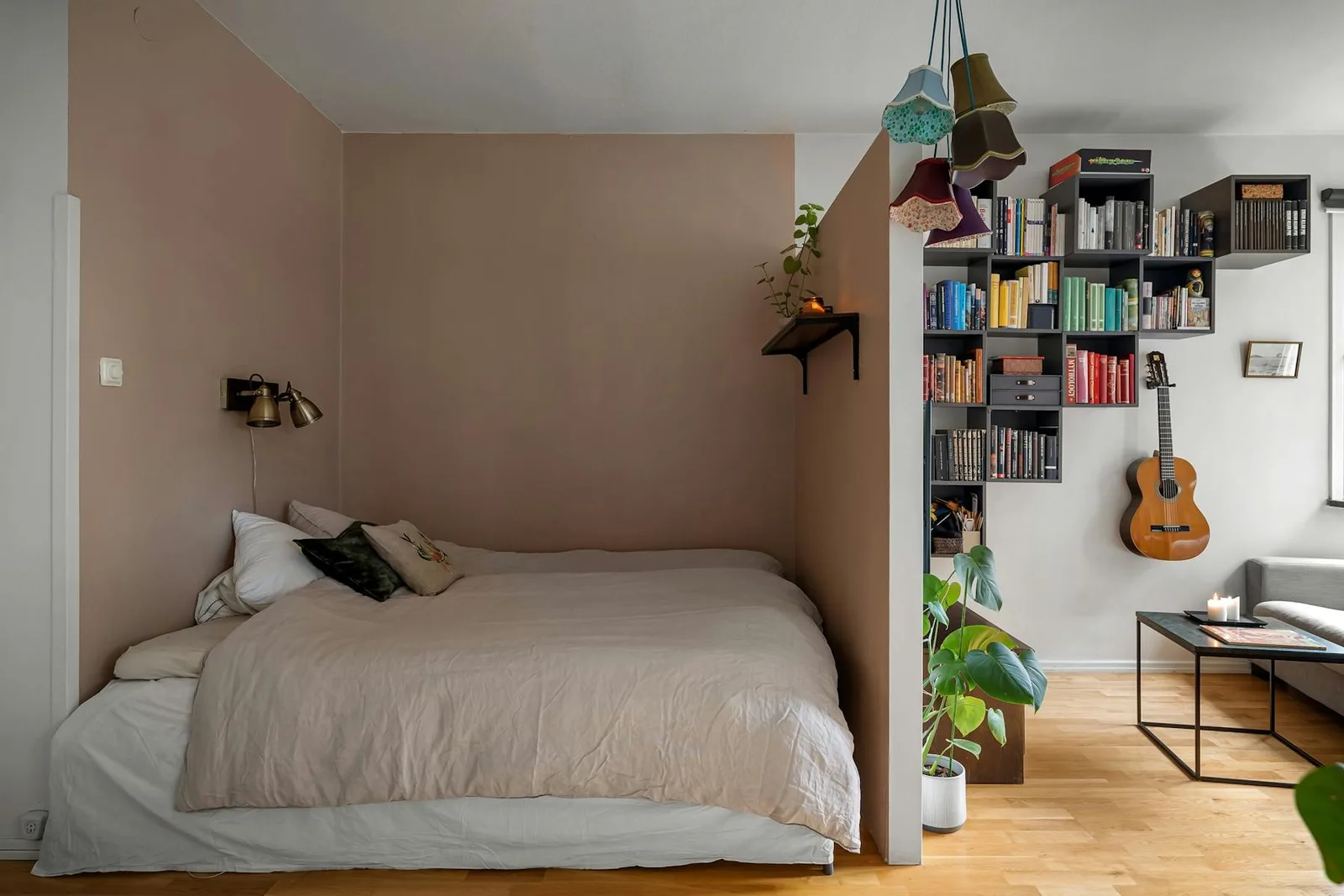 Studio apartment bed tucked behind a partial wall with living area and shelving beside it