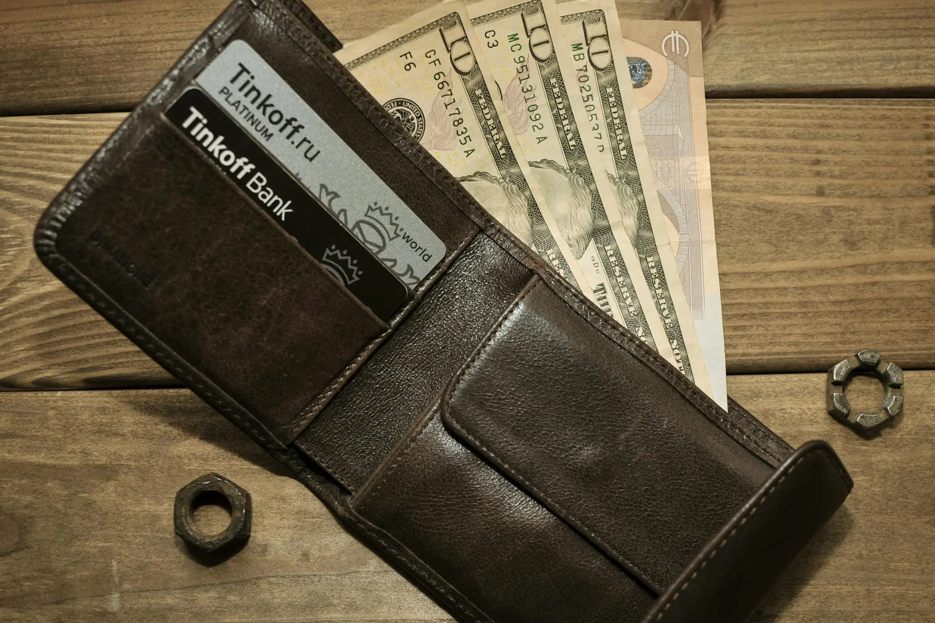 Brown wallet holding cash and cards on a wood surface