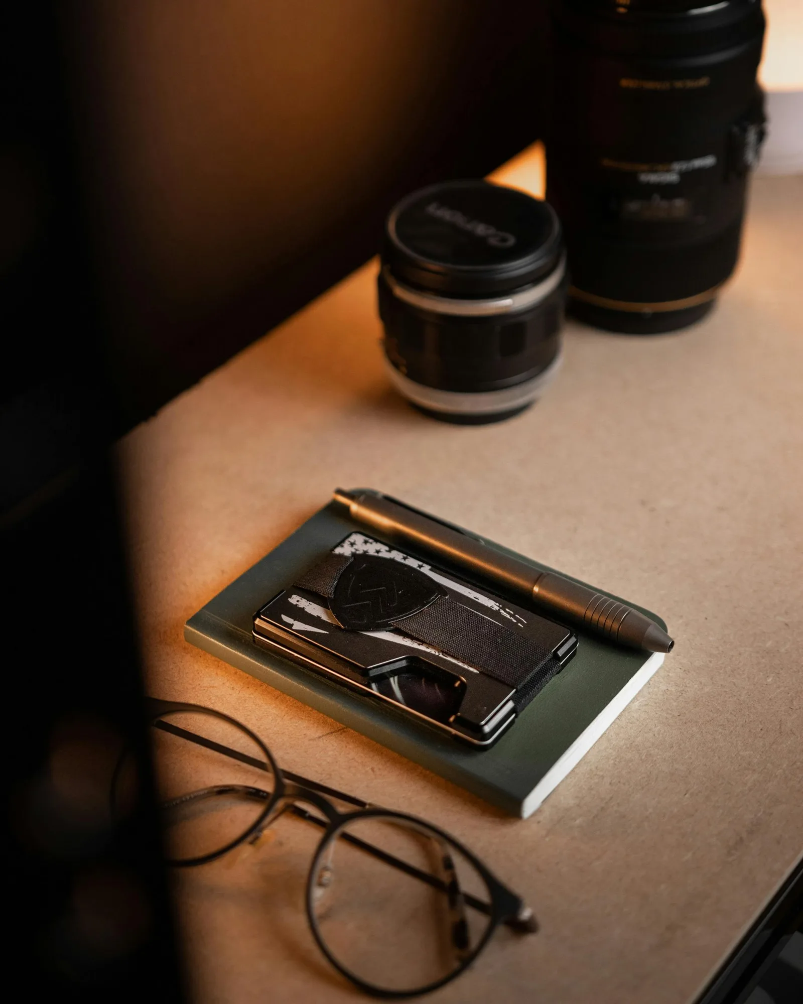 Dark wallet resting on a notebook beside camera lenses in warm light