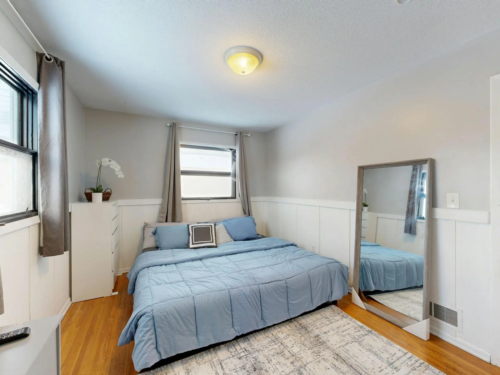 Small bedroom with pale blue bedding, white walls, and warm wood flooring