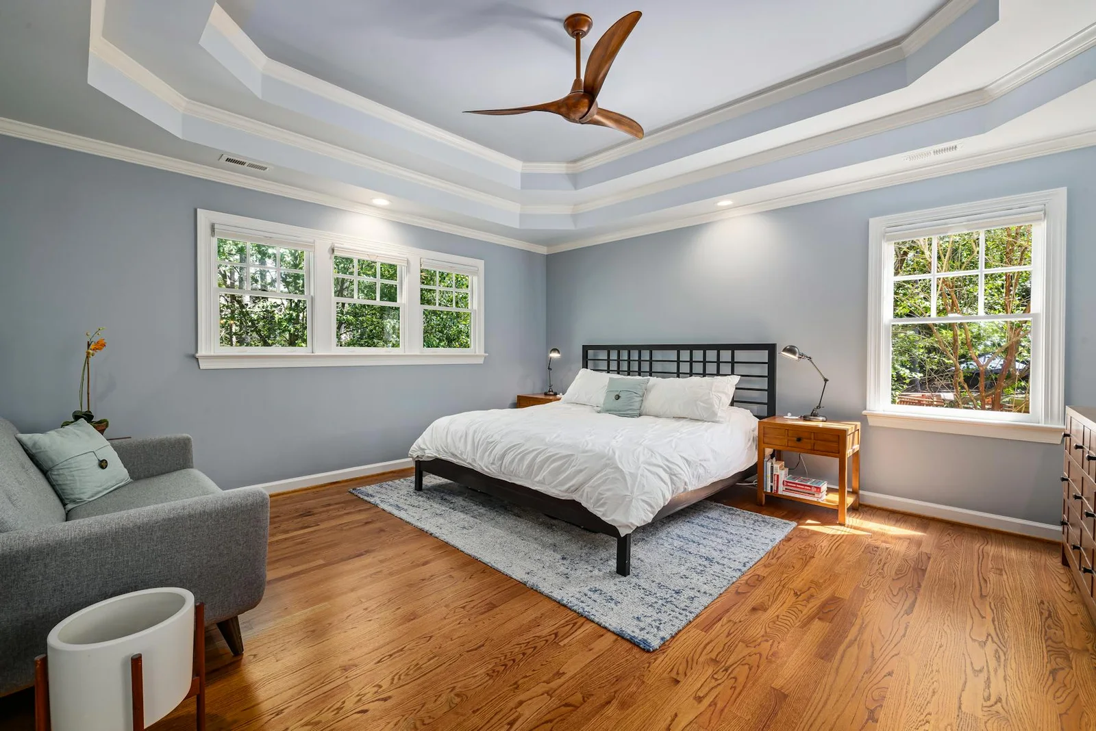 Bedroom with soft blue ceiling detail, wide windows, and warm wood flooring