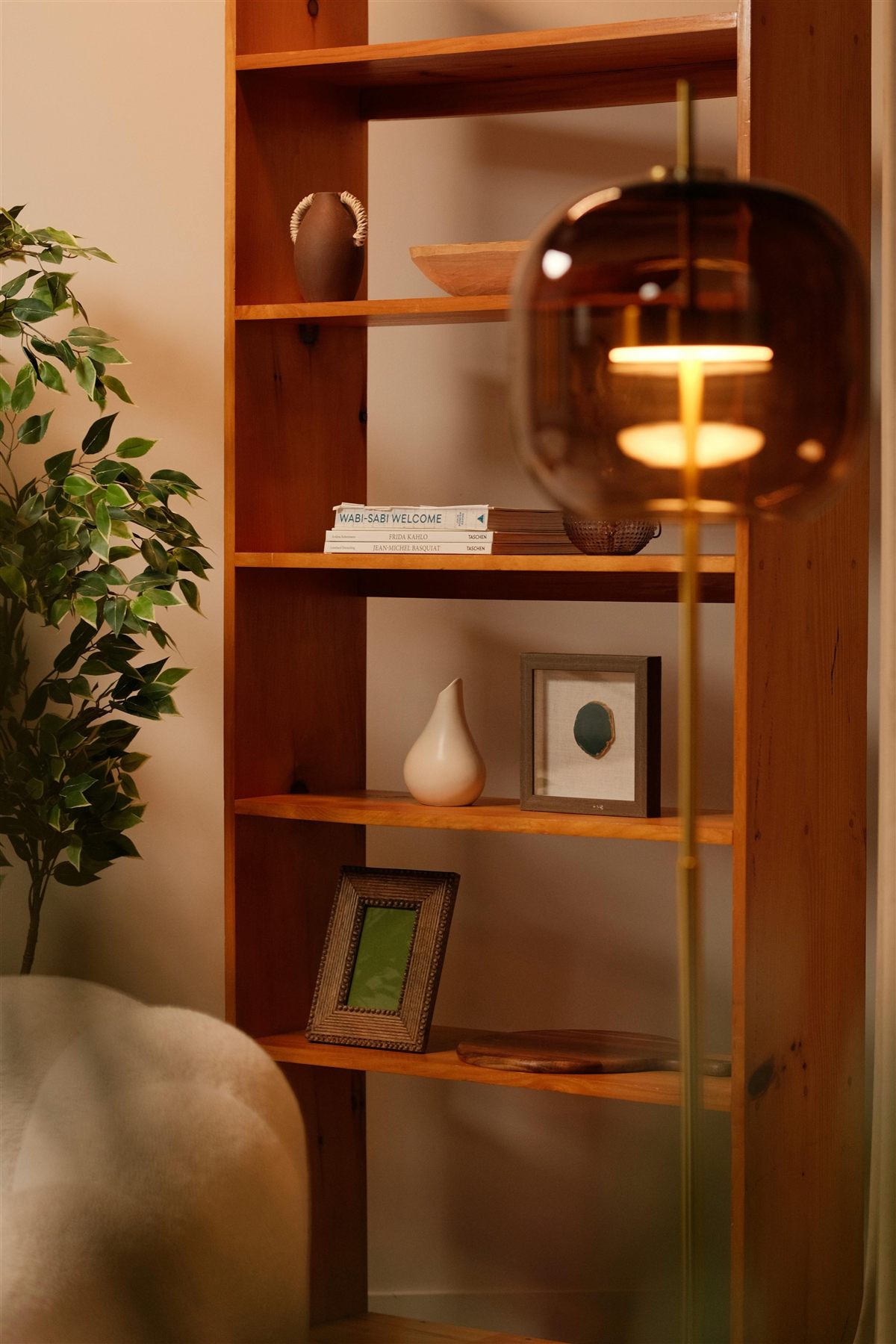 Wood shelf with warm lamp, framed art, books, and a plant