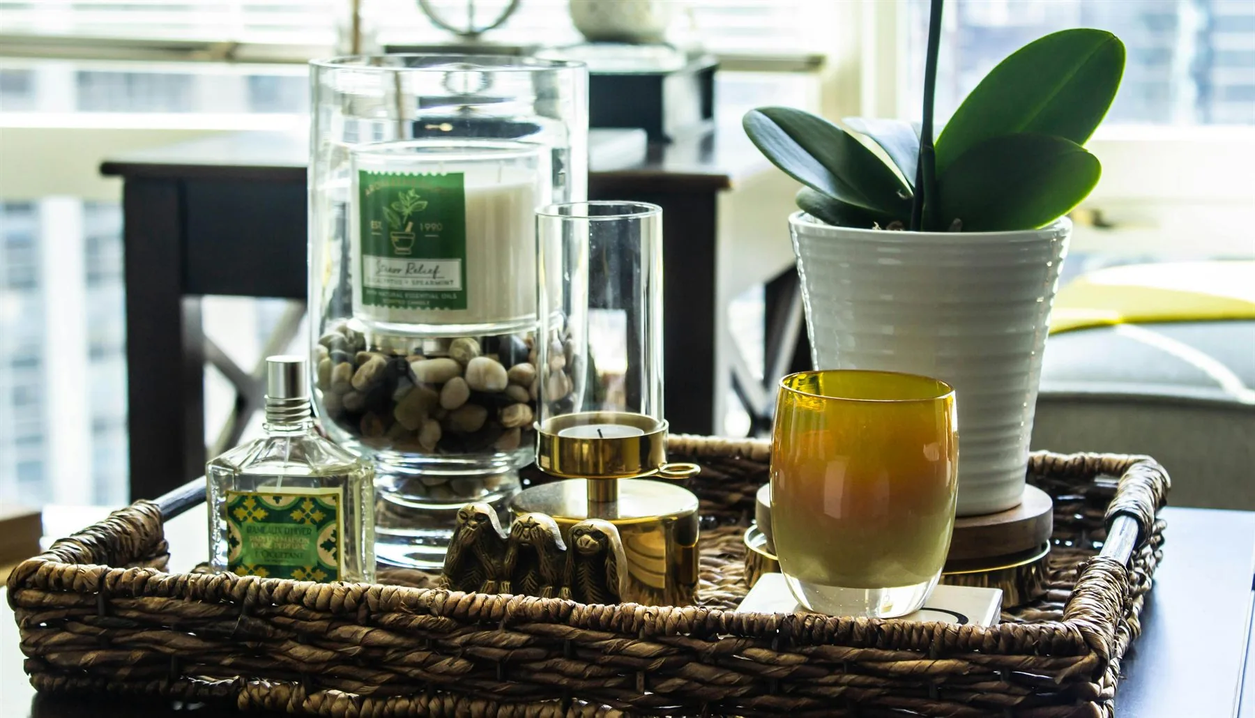 Woven tray with plant, candle, and small decor pieces by a window