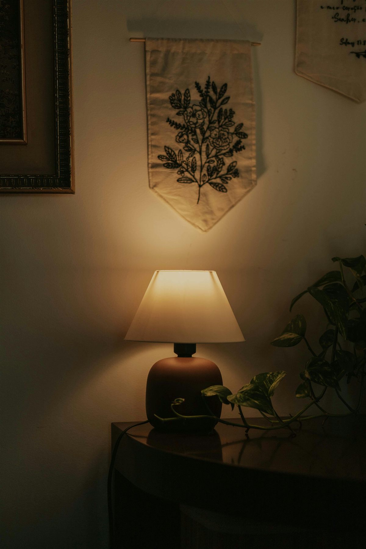 Warm lamp on a table with textile wall art and plant nearby