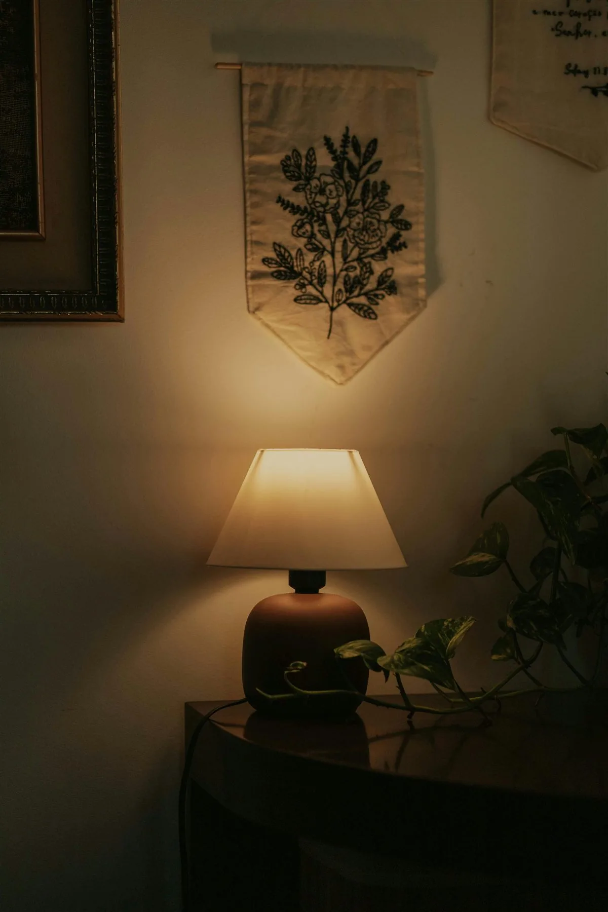 Warm lamp on a table with wall textile and plant nearby