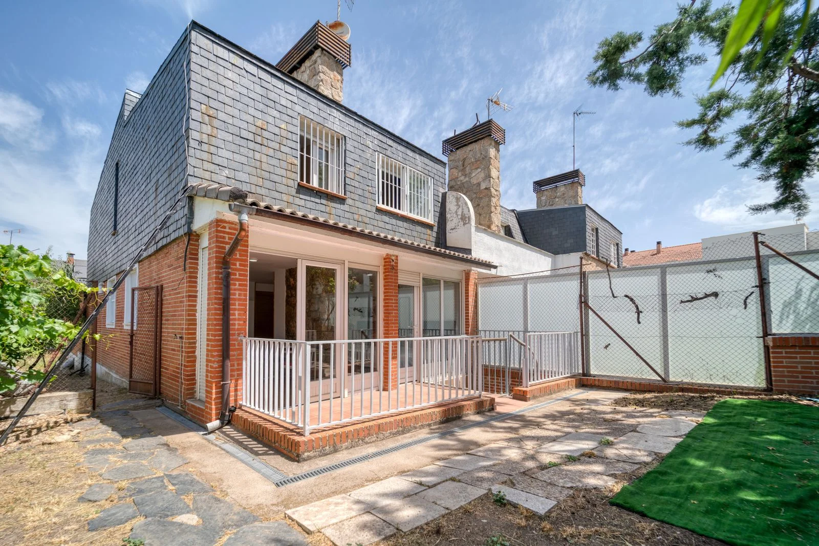 Red brick house with dark upper cladding and a covered paved rear patio