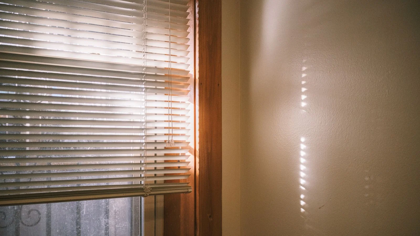 Direct sunlight passing through horizontal window blinds onto an interior wall