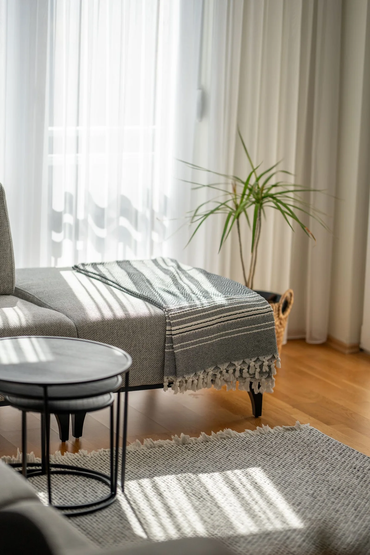 Living-room seating beside sheer and heavier curtains with compact nesting tables