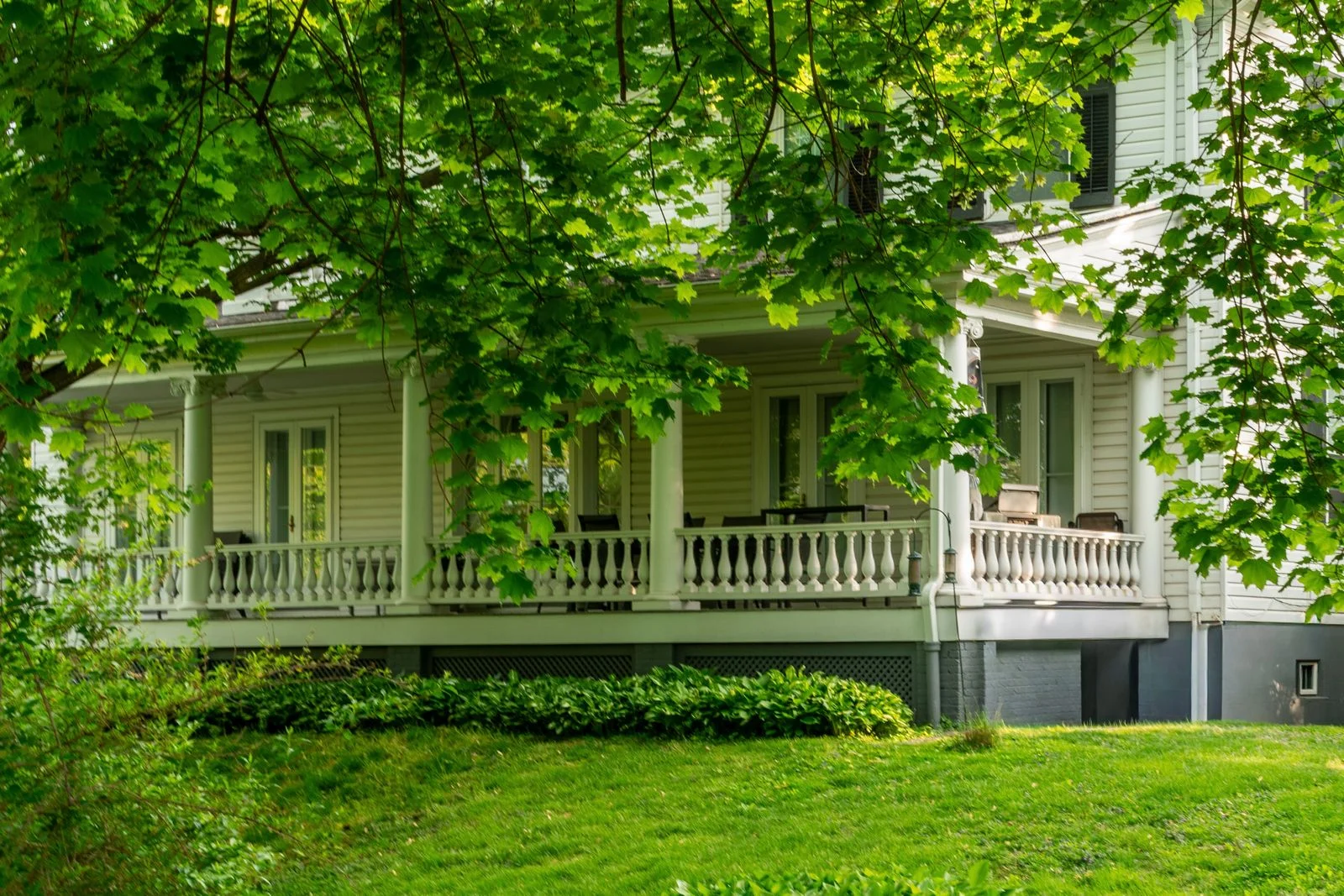 White house with a covered porch and a clear approach surrounded by green trees