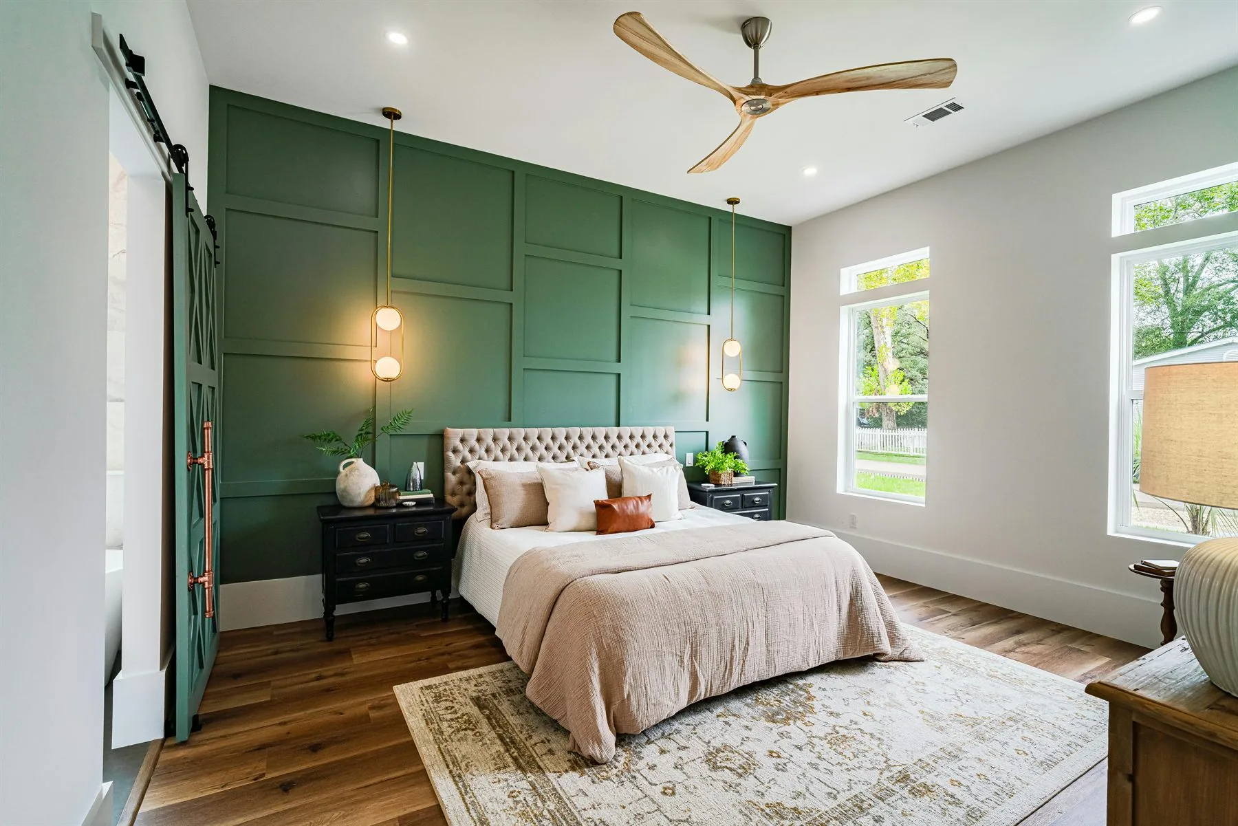 Bedroom with a deep green paneled wall, soft neutral bed, wood floor, and warm bedside lamps